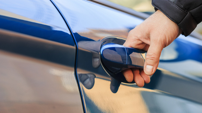 a hand reaches for the handle of a blue car door