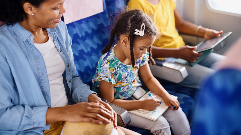 Young girl coloring during a flight as mother watches on