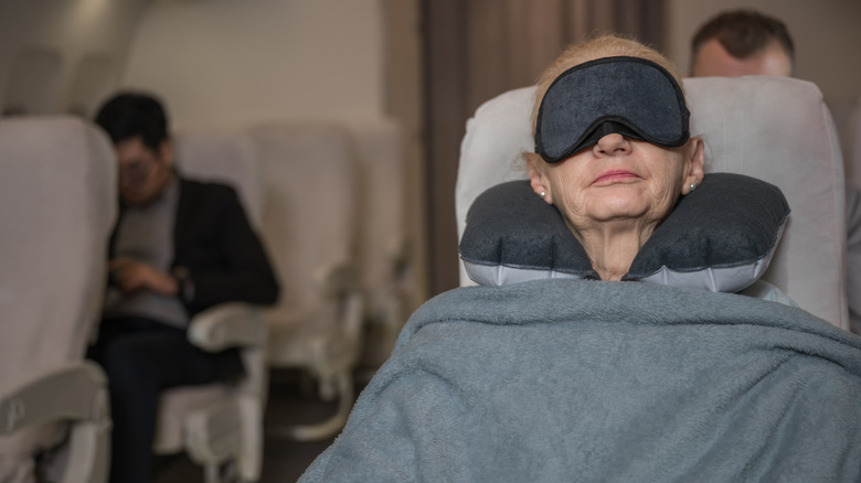 Old woman sleeping with eye mask, neck pillow, and blanket on a flight