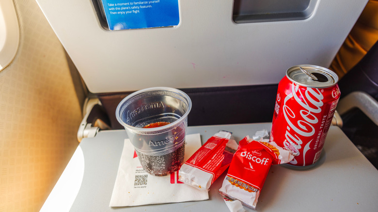 Cup of soda, a can, and snacks on a flight tray table