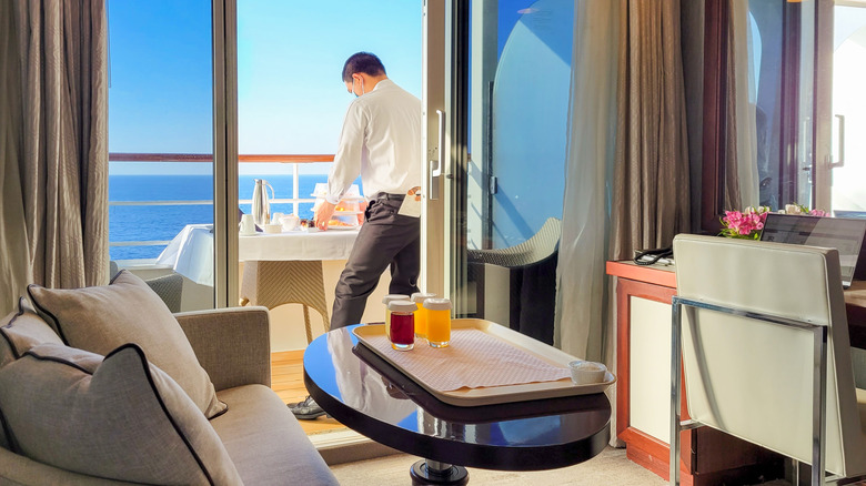 A server delivers a full breakfast via room service on a stateroom balcony with the blue Mediterranean Sea in view on a cruise ship