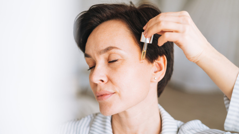 A woman applies oil to her face with a dropper