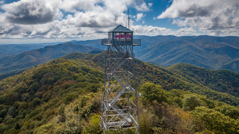 A graffitied steel tower, Frying Pan Lookout Tower, on top of green mountains with a cloudy sky