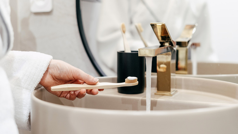 A woman holding a toothbrush under the running water in a hotel bathroom