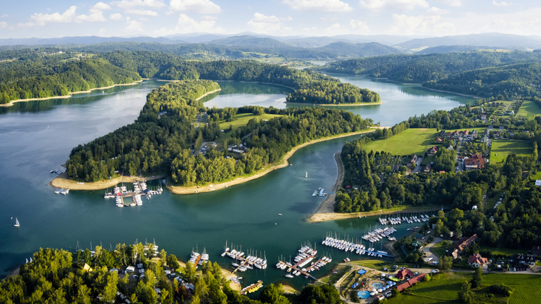 Aerial view of Lake Solina, with boats on the port, hills in the background, and trees surrounded by blue waters.