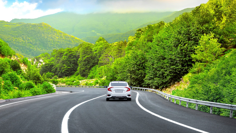 Landscape image of a white car driving along a highway