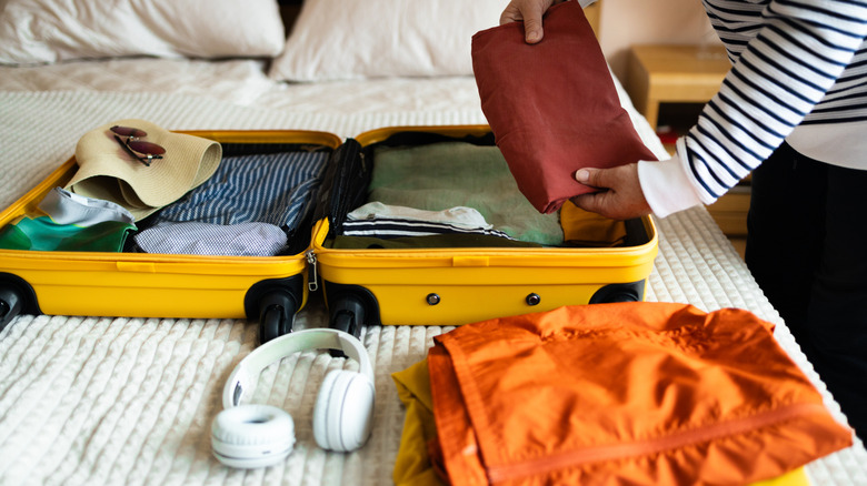Person with an open suitcase on a bed, packing for vacation