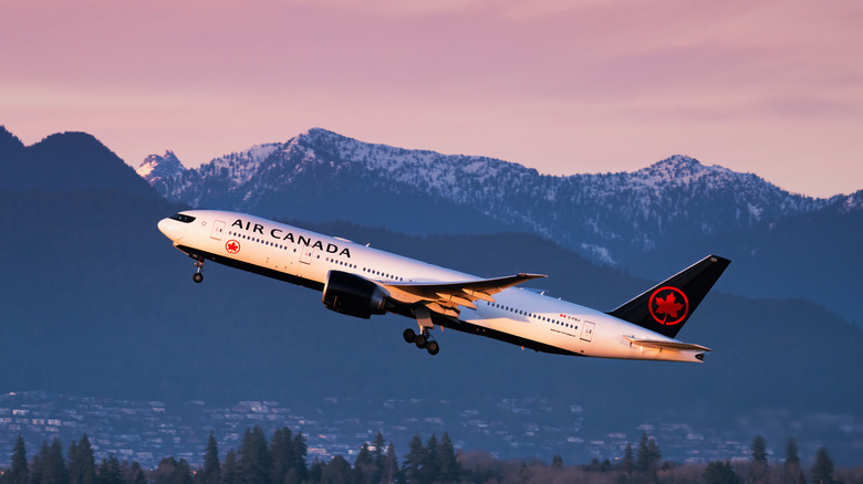 An Air Canada plane taking off against a backdrop of mountains bathed in a soft pink light from sunrise or sunset