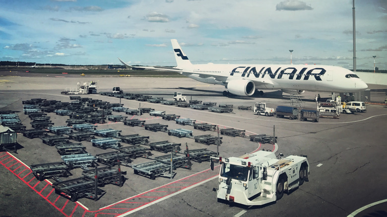 Aerial view of a Finnair airplane on the ground in Helsinki's Vantaa Airport, with various service vehicles and equipment around.