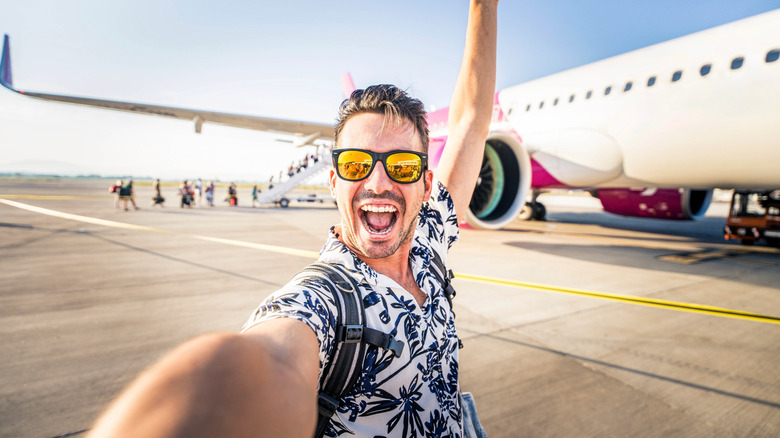 Happy male traveler posing in front of plane