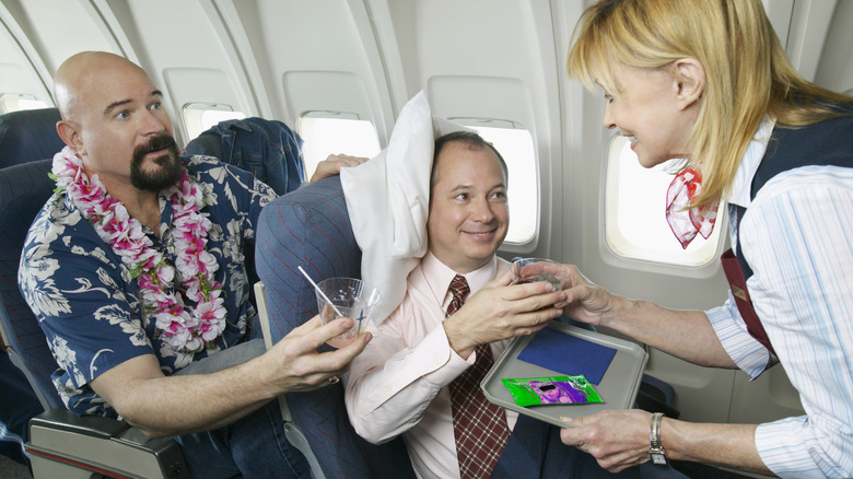 passenger handing flight attendant empty cup while they serve another passenger a beverage