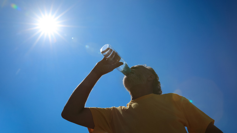 low angle shot of an older man drinking water with the sun above him