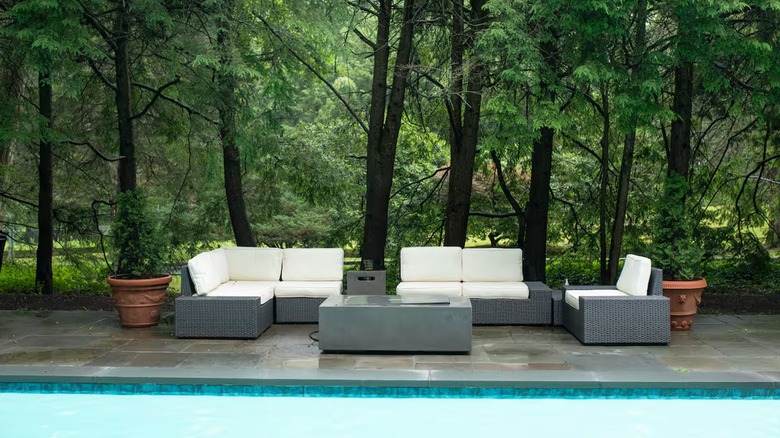 An outdoor lounge suite by the swimming pool with the beautiful gardens and woods in the background