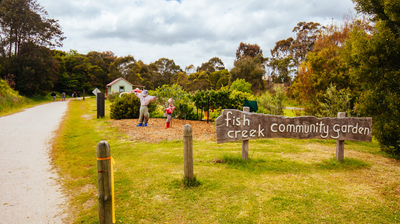 Entrance to the Fish Creek Community Garden with trees surrounding and two scarecrows out front