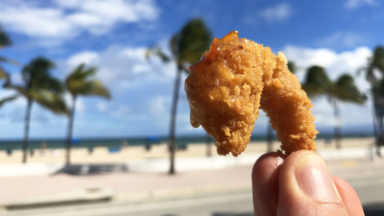 Person holding a fried shrimp in front of a Florida beach
