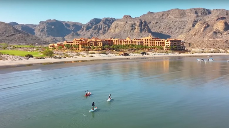 Kayakers and paddleboarders in front of a hotel backed by rugged hills in Baja, California