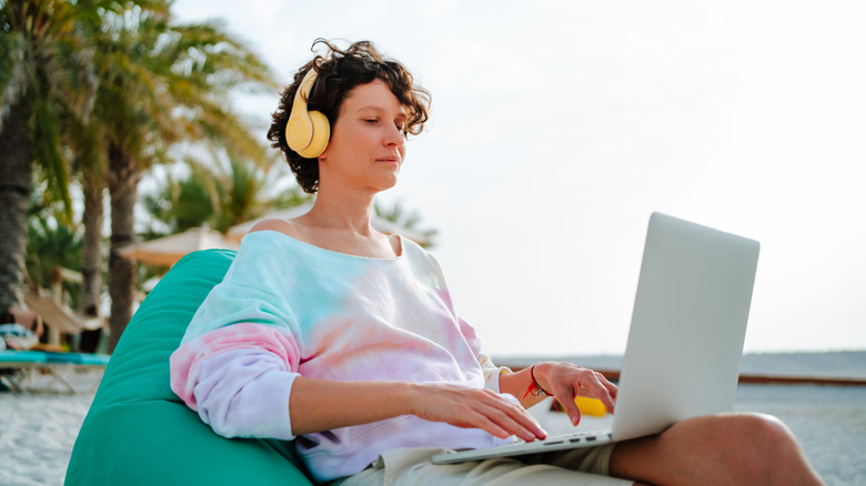 A woman in earphones with a laptop working on the beach