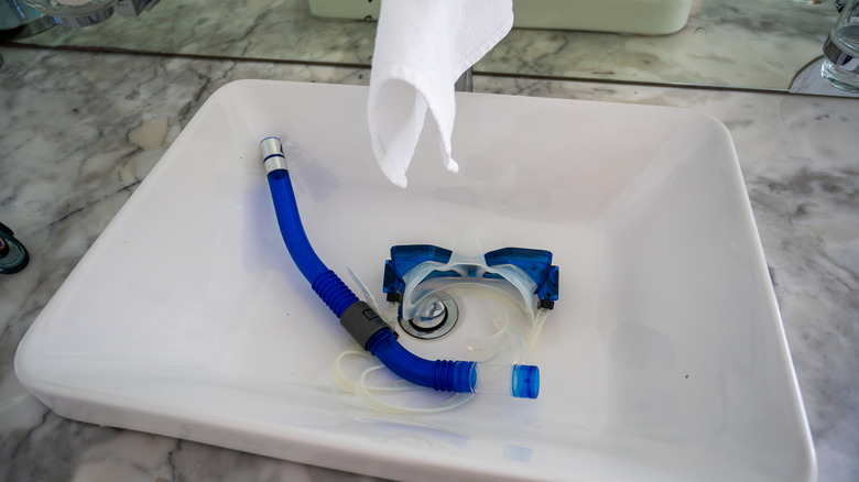 A snorkeling mask in a sink and a washcloth on the nozzle