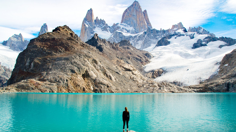 Hiker standing in front of glacial lake overlooking towering mountain cliffs in Patagonia