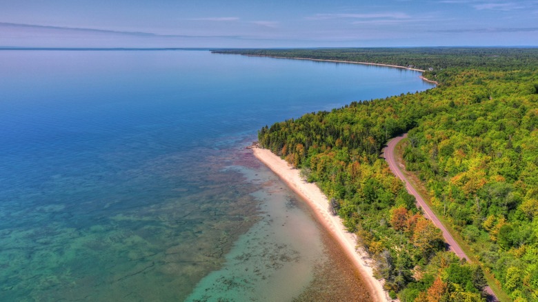 An aerial photo showing the sandy beach at Brunette Park, the road cutting through the forest behind it, the Keweenaw Peninsula to the right and the clear water of Lake Superior to the left