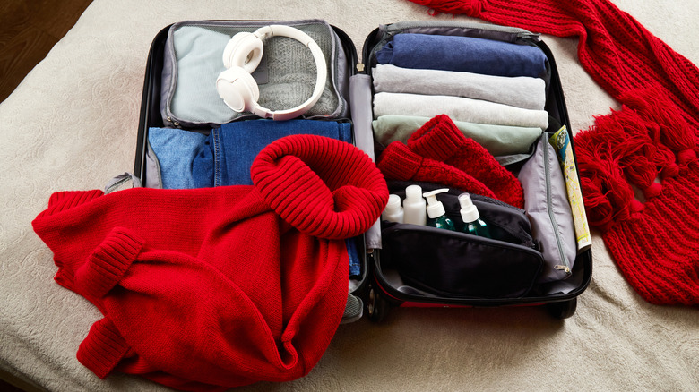 packing a suitcase with winterwear, toiletries, and other clothing