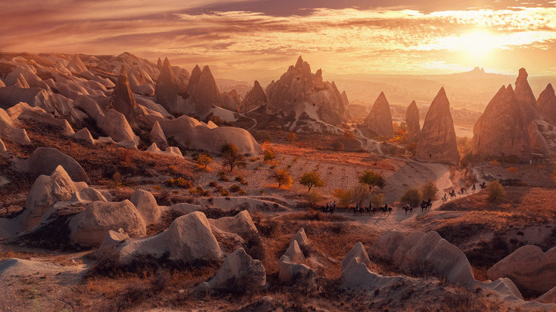 A group rides horses through an arid landscape at sunset