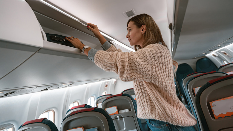 A woman reaching her hands into an overhead bin on an airplane
