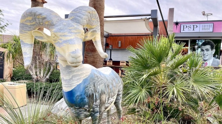 A mountain goat sculpture in a garden courtyard with a coffee house at Palm Springs International Airport.