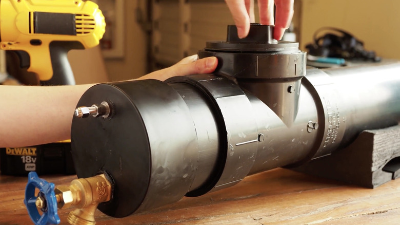 A person's hands creating a DIY solar-powered shower with a pipe on a wooden tabletop