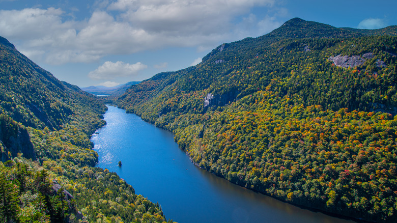 Aerial view of a narrow lake between two high peaks covered in trees in Adirondack Park