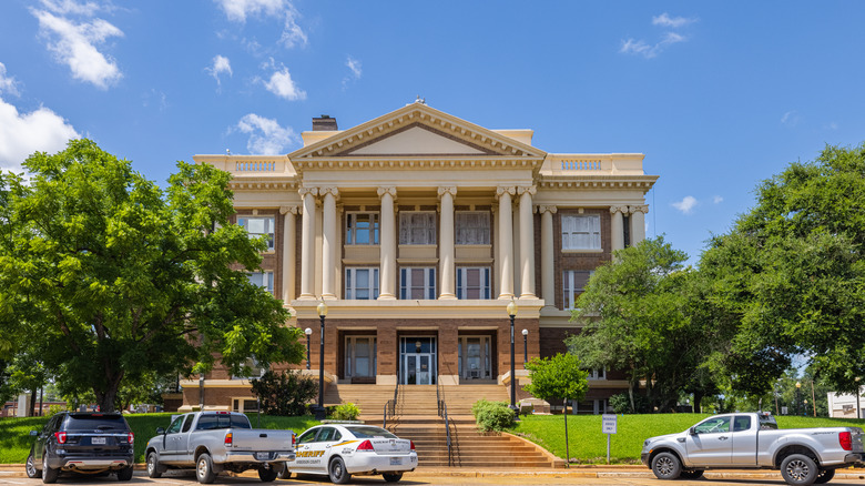 A light stone courthouse with four pillars and a parking lot in front