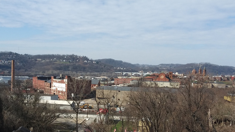 View from Melwood Avenue Overlook, with treed hills, bridge, and red brick buildings under cloudy blue sky