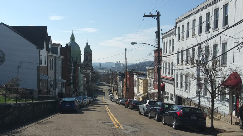 Homes and cars line street in Polish Hill against green church domes in front of view of Pittsburgh
