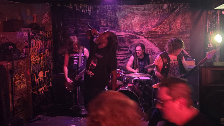 Punk band in black attire performing at Rock Room before graffiti and waterfall backdrop