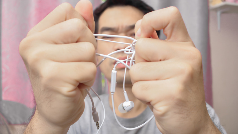 A frustrated traveler trying to untangle white headphones.