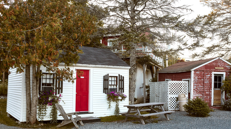 picnic tables in front of white house with red door under tall trees under overcast sky