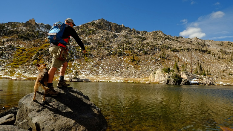 Man with dog fishing from boulder at mountain lake