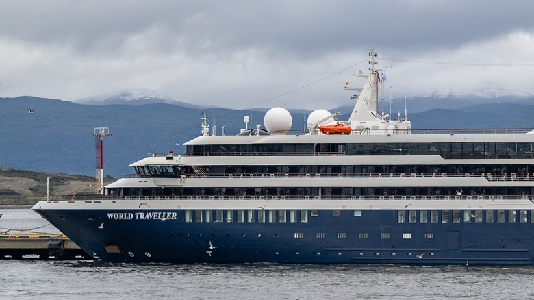 The front of Atlas Ocean Voyages' cruise ship, World Traveller docked under a cloudy sky.