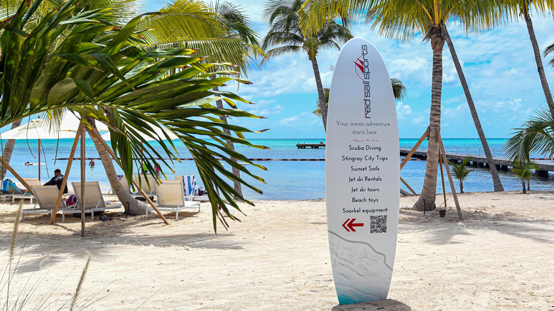 A sign printed on a surf board propped up in the sand at Rum Point, Grand Cayman