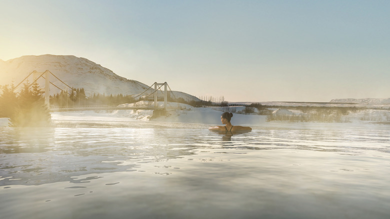 woman in a thermal pool overlooking a bridge and snowy landscape