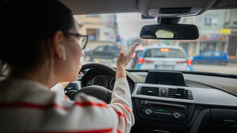 A woman with earpods gesturing at the traffic ahead of her