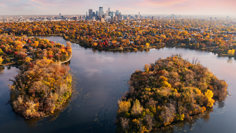 An aerial view of Minneapolis in the fall, lake and trees in the foreground with downtown buildings behind