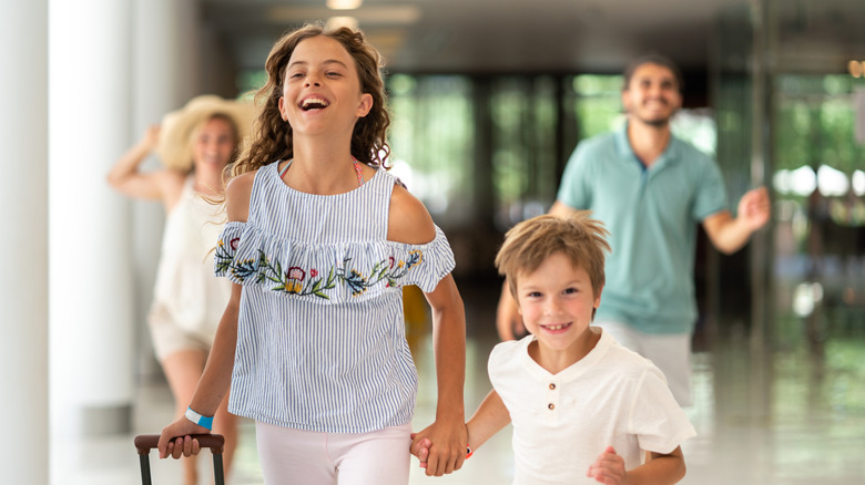 Children running excitedly through an airport with their parents smiling in the background
