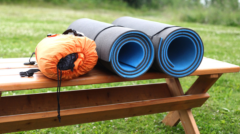 Rolled yoga mats on a bench next to a bag of camping gear.