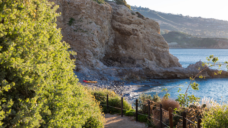 Secluded cliffside hiking trail with small, empty shoreline with one kayak on the rocks during the day.