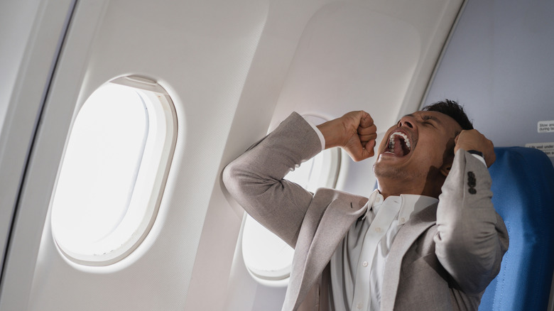 A man in a business suit screaming in his seat on an airplane