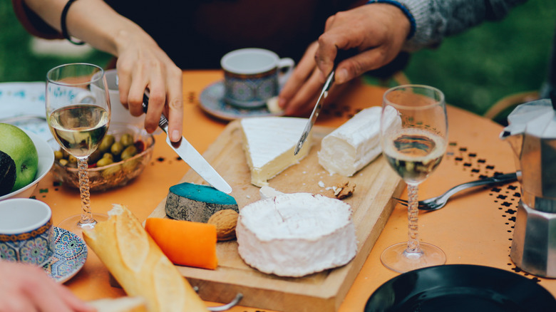Dinner guests using knives to cut into French cheeses