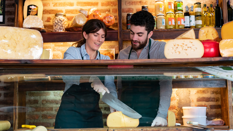 Two people in France cutting cheese at a market counter for customers