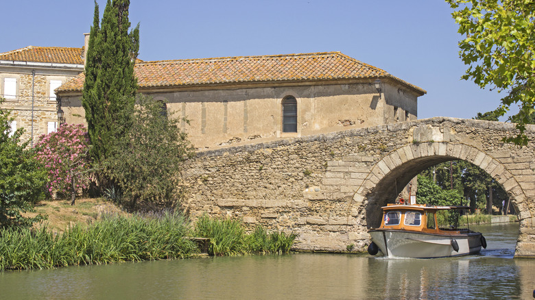 A boat passing under a stone bridge on the Canal du Midi in Le Somail, France