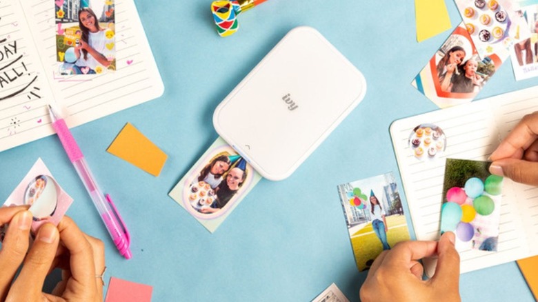 Two pairs of hands are holding stickers created from the Canon IVY 2 Mini Photo Printer, a compact and portable printer that connects to your smartphone.
